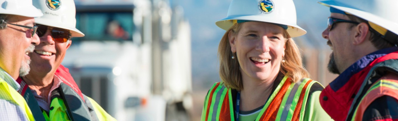 men and women in hard hats and safety vests talk outside
