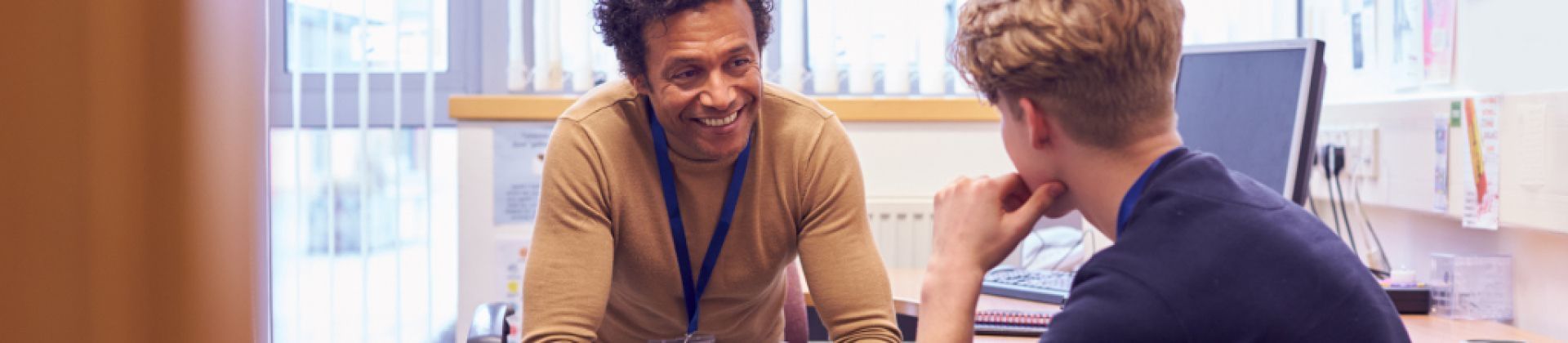 man sitting at desk smiling at adolescent boy facing him